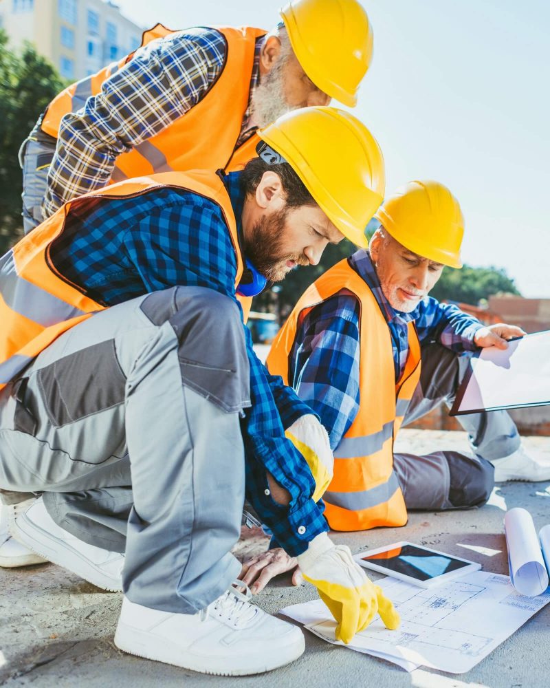 handsome-construction-workers-sitting-on-concrete-at-construction-site-discussing-building-plans-1.jpg